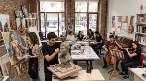 Art students in a studio painting, sculpting, and playing instruments around a bright, brick-walled room with large windows.